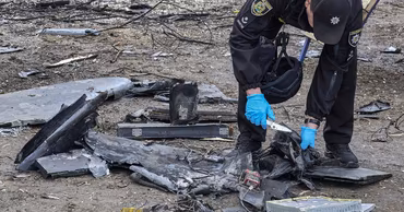A Ukrainian police officer examines the charred wreckage of a downed drone on the ground.