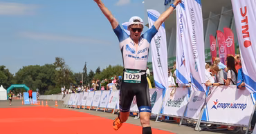 A triathlete crossing the finish line with arms raised at a sports competition.
