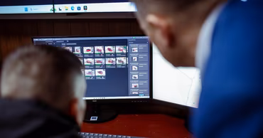 Two people looking at computer monitors displaying surveillance or data monitoring software.