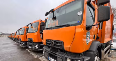 A row of orange waste collection trucks parked in a lot.