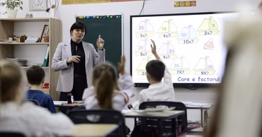 A teacher instructing students in a classroom with an interactive whiteboard.