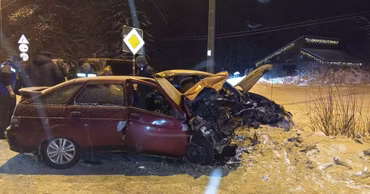 A badly damaged red car at night after a head-on collision on a snowy road.
