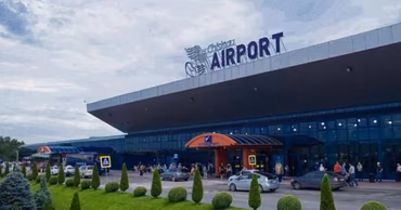 Exterior view of the Chisinau International Airport terminal building with cars and passengers.