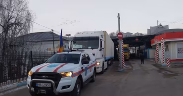 A Moldovan police vehicle escorting a large truck carrying humanitarian aid at a border crossing.