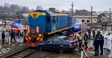 A blue car damaged after colliding with a locomotive at a railway crossing with emergency services present.