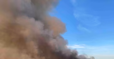 A large fire with thick smoke rising from a landfill site in Orhei with a bulldozer nearby.