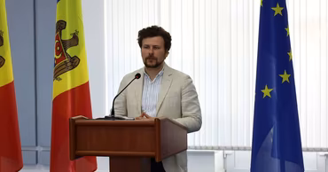 Dan Perciun, Minister of Education of Moldova, speaking at a podium with flags in the background.