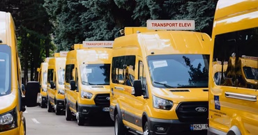 A row of yellow school buses parked in a line, labeled Transport Elevi.