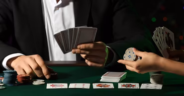 People playing cards and handling casino chips at a green table.