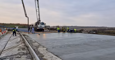 Construction workers pouring concrete on a road surface with a concrete pump truck.