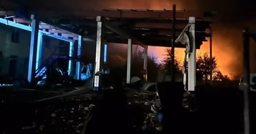 A damaged border crossing facility at night with fire in the background.