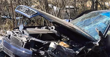 A heavily damaged black Audi car after a road accident in a wooded area.