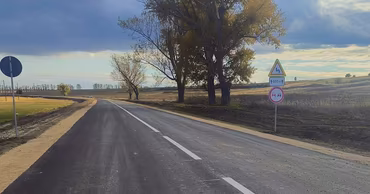 A paved road in the countryside with traffic signs under a cloudy sky.