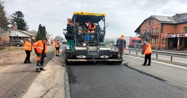 Workers in orange vests operating a road paver machine on a construction site.