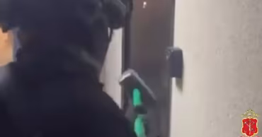 A police officer in tactical gear breaching a door during an operation.