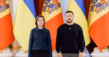 Maia Sandu and Volodymyr Zelenskyy standing together in front of Moldovan and Ukrainian flags.