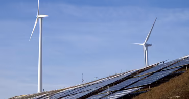 Wind turbines and solar panels installed on a hillside under a clear blue sky.