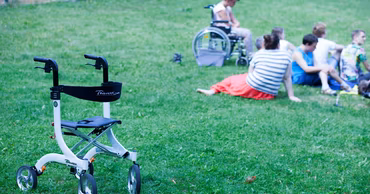 A mobility walker in the foreground with a group of people sitting on the grass.