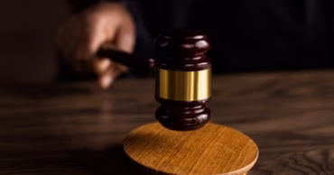 A wooden judge's gavel striking a sounding block on a dark wooden table.