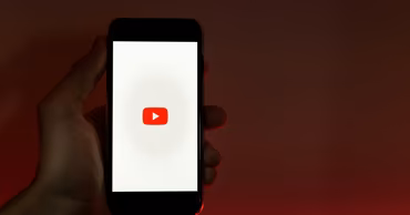 A hand holding a smartphone displaying the YouTube logo on the screen.