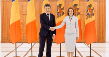 Nicusor Dan and Maia Sandu shaking hands in front of Moldovan flags.