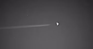 A black and white image showing a triangular object in the sky with a trail.