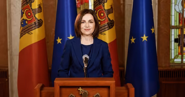 President Maia Sandu speaking at a podium with Moldovan and European Union flags in the background.