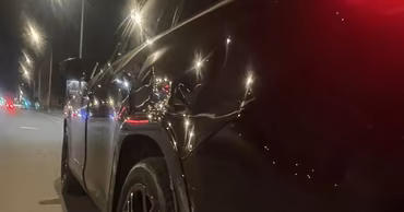 A damaged black car parked on a city street at night.