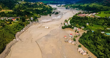 Aerial view of a flooded river valley in Nepal with damaged houses and mud.