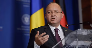 Romanian official speaking at a podium with the Romanian flag in the background.