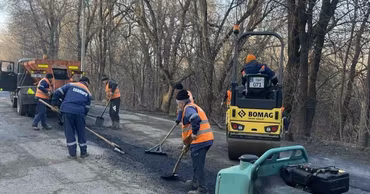 Road workers in orange vests using machinery to repair asphalt on a road.