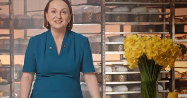 EU Ambassador Ivona Piurow standing in a bakery setting with flowers and Easter cakes.