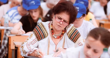 A woman in a traditional Moldovan blouse writing at a desk during a dictation event.