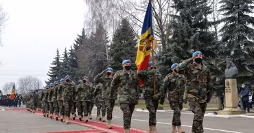 Moldovan soldiers in camouflage uniforms marching with the national flag during a military ceremony.
