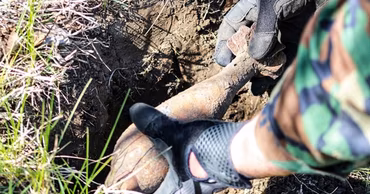 A Moldovan sapper in camouflage uniform removing an old unexploded mortar shell from the ground.