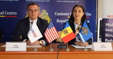 Radu Vrabie and Lidia Ababii sitting at a table with flags during a Customs Service event.