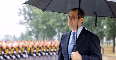 Vasile Tofan holding an umbrella at an official ceremony with soldiers in the background.