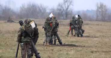 Soldiers in camouflage uniforms conducting mortar training exercises in an open field.