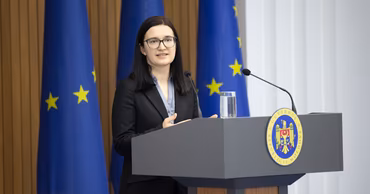 Cristina Gherasimov speaking at a podium with Moldovan and EU flags in the background.