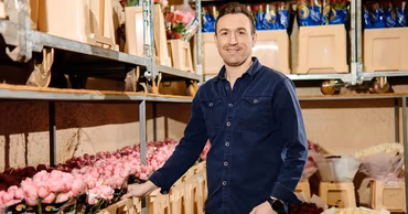 A man standing in a flower warehouse, representing a small business owner.