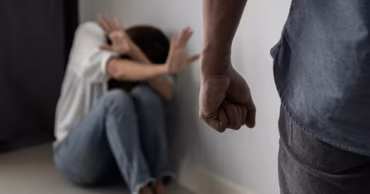 A man with a clenched fist standing over a woman cowering in a corner.