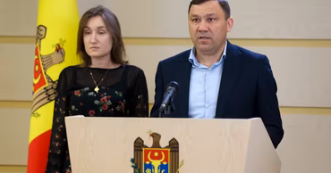 Vasile Gradinaru speaking at a press conference with the Moldovan flag in the background.