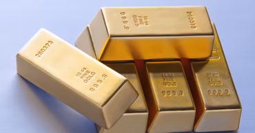 Several shiny gold bars stacked on a light blue background.