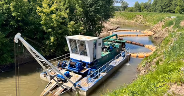 A dredger machine working on cleaning a riverbed in a natural environment.