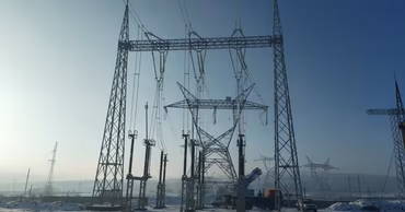 High-voltage power line towers under construction in a snowy field.