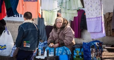 An elderly woman sitting at an outdoor market in Moldova, representing economic struggle.
