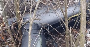 Wreckage of a crashed drone lying in a wooded area with light snow on the ground.