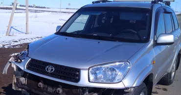 A damaged silver Toyota RAV4 parked on the side of a road.