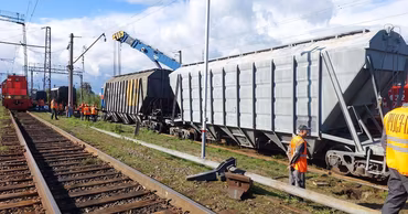 Freight train cars derailed on tracks with workers and a crane at the scene.