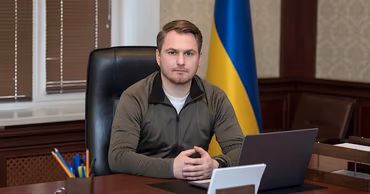 Ruslan Kravchenko sitting at his desk with a Ukrainian flag in the background.